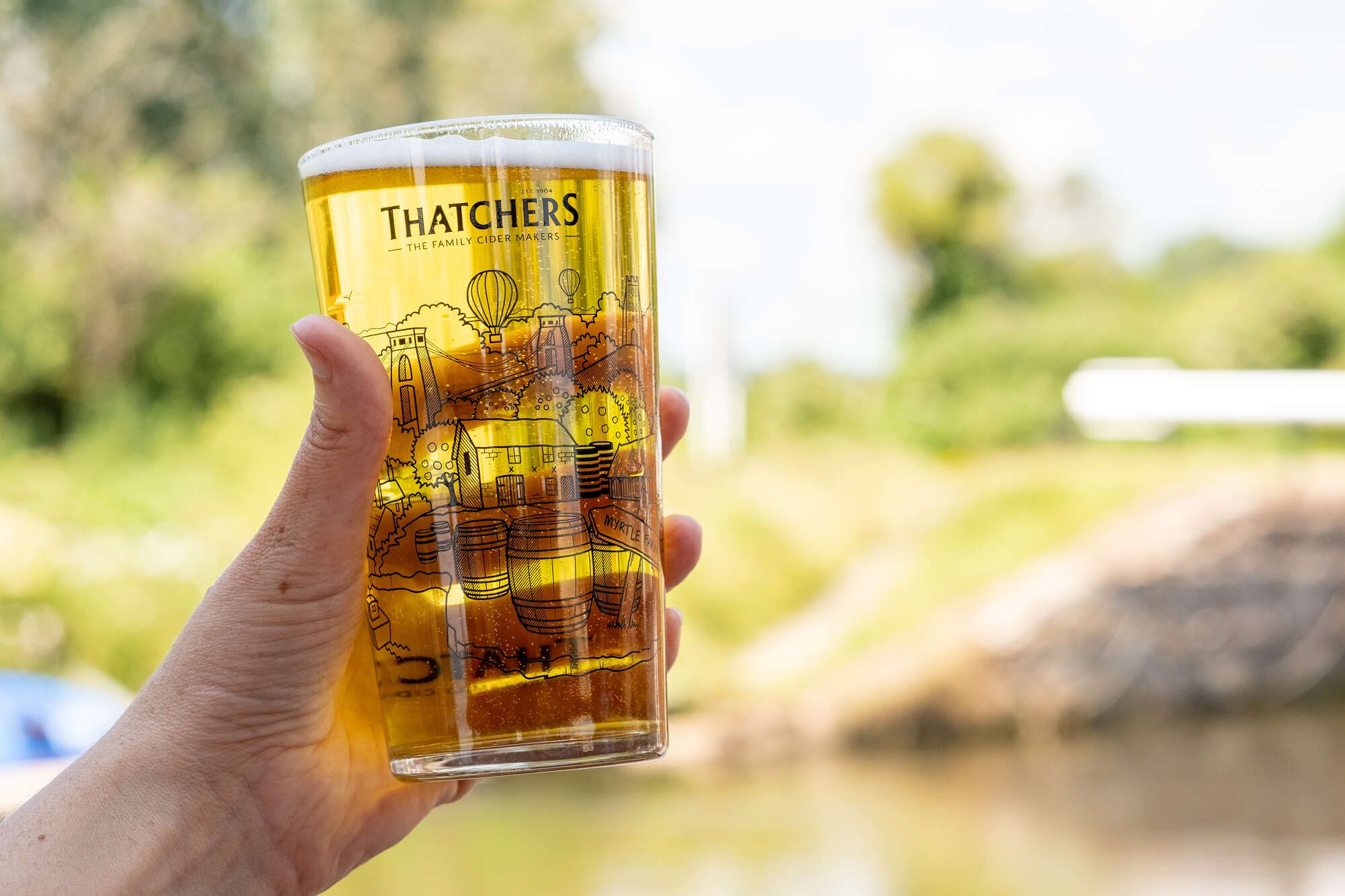 A pint of Thatcher's Cider being held to the light out near the River