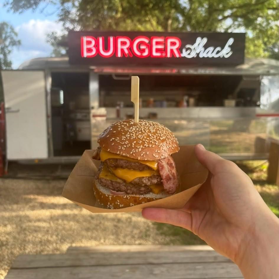 Burger Shack in the background with someone holding a juicy burger in the foreground